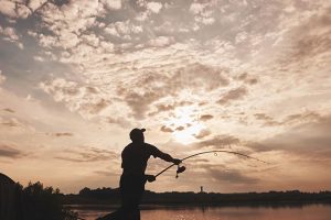 Bild eines Anglers im Sonnenuntergang, der die Angelrute auswirft.